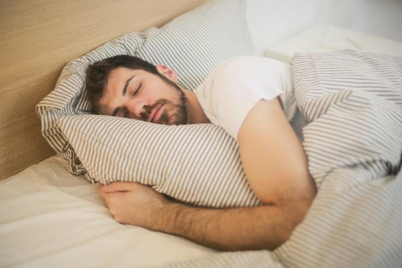 A man sleeps in bed, hugging a stripy duvet